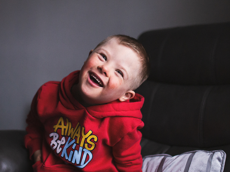 a boy wearing a 'always be kind' red jumper smiling