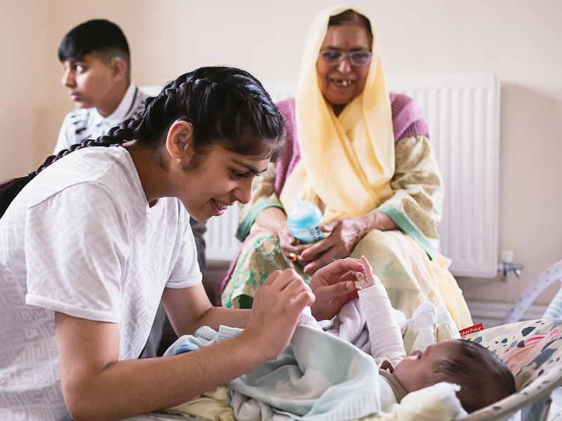 a girl playing with her baby sister while their brother and grandma look over them