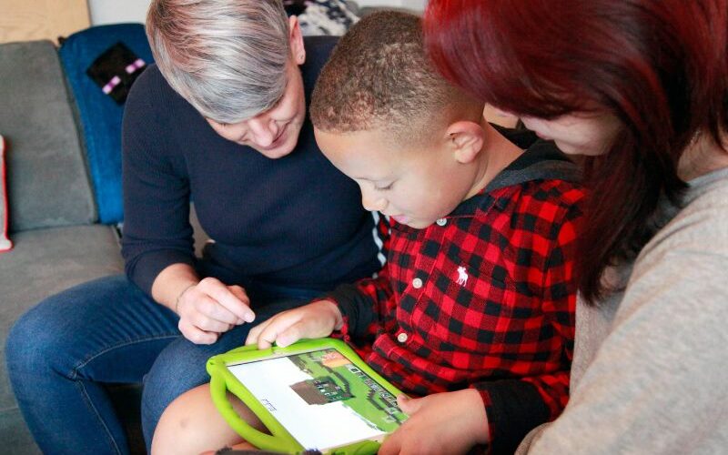 A boy using his iPad tablet with his mum and sister either side of him