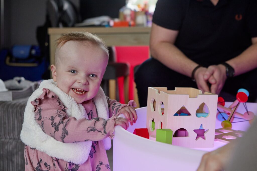 Baby holds on to sensory toys and grins at the camera.