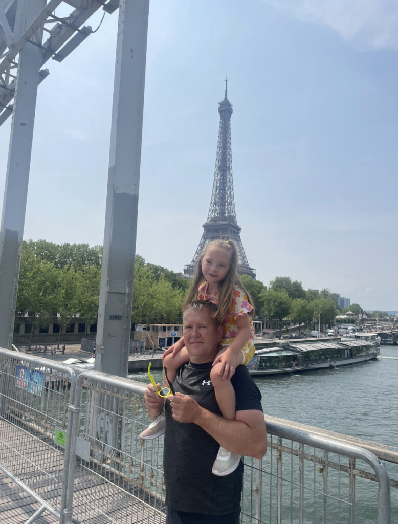 Dad carries daughter on shoulders in front of Eiffel Tower