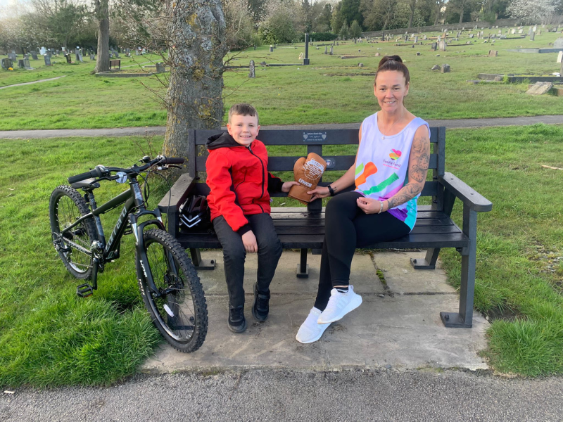 Donna and Adam sit on Ryan's memorial bench. They are holding the champion's golden boxing glove.