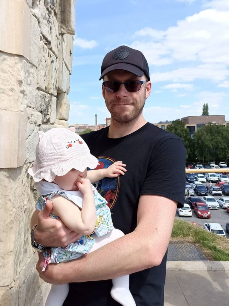 A photo of Nathan holding his daughter and smiling.