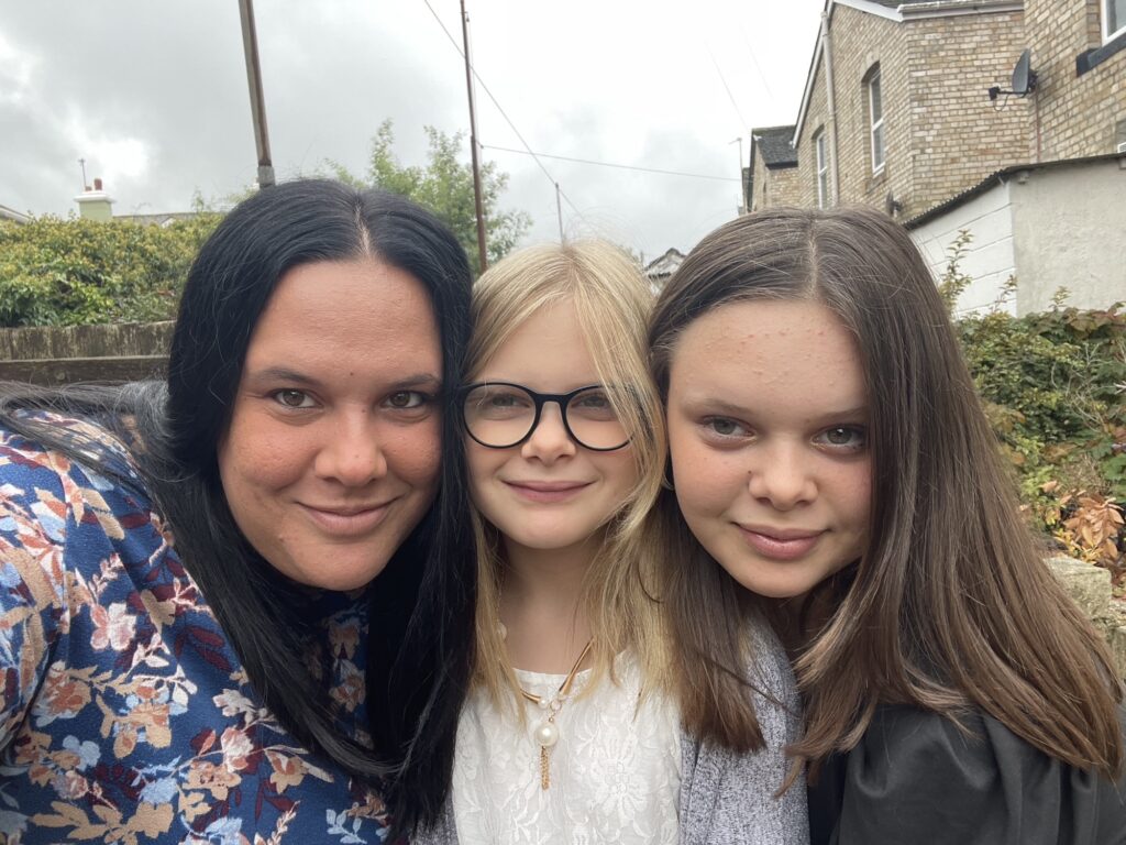 Sam, Molly and Lucy are all looking at the camera and smiling. Sam is taking the photo, and all of their faces are pressed to one another. They are outdoors.