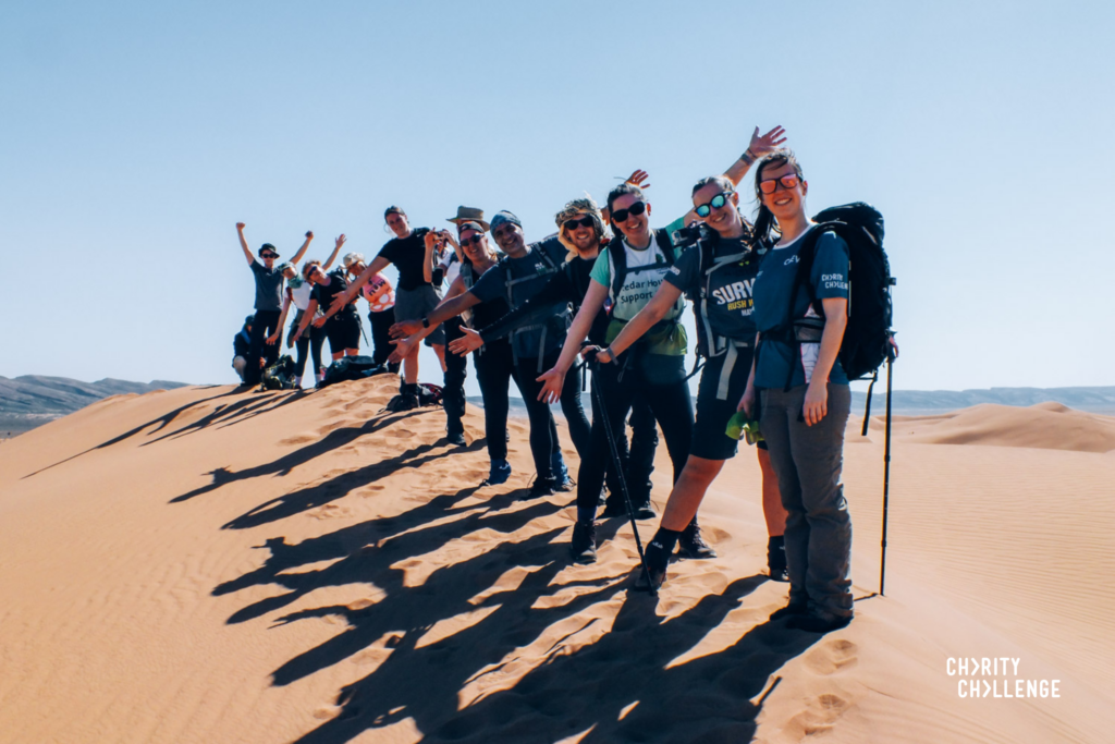 A group of happy people stood on a sand dune in the Sahara Desert taking part in the Sahara Trek charity challenge.
