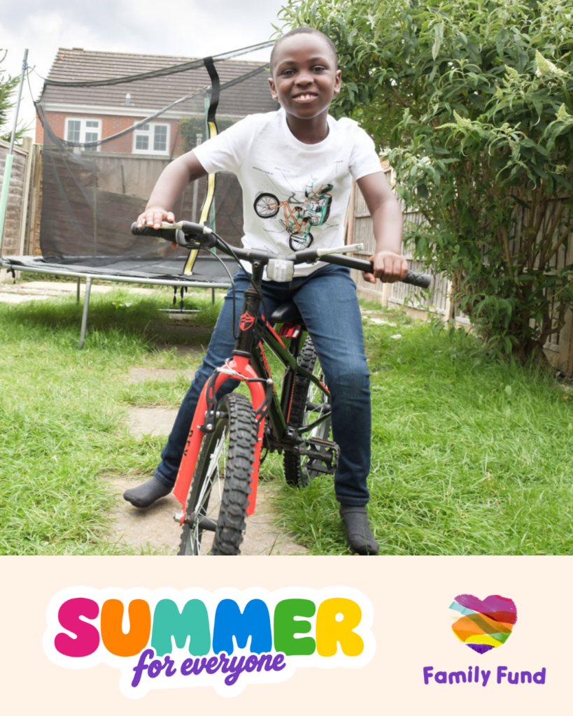 A young boy sits on his bike in a garden smiling at the camera. A banner at the bottom has two logos that say 'Summer for everyone' and 'Family Fund'