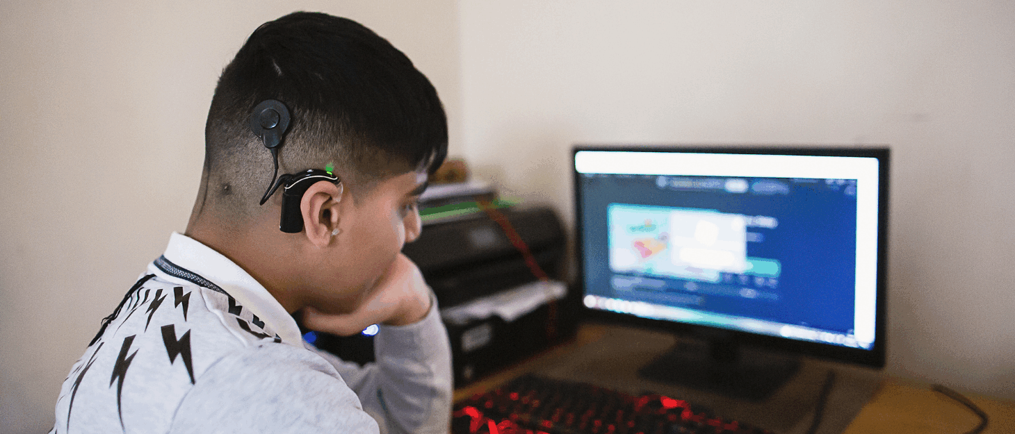 A boy wearing a hearing aid and looking at a computer