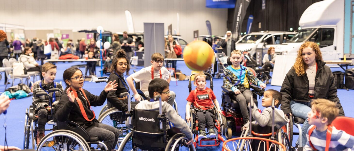 A group of children in wheelchairs playing wheelchair basketball in a large exhibition hall