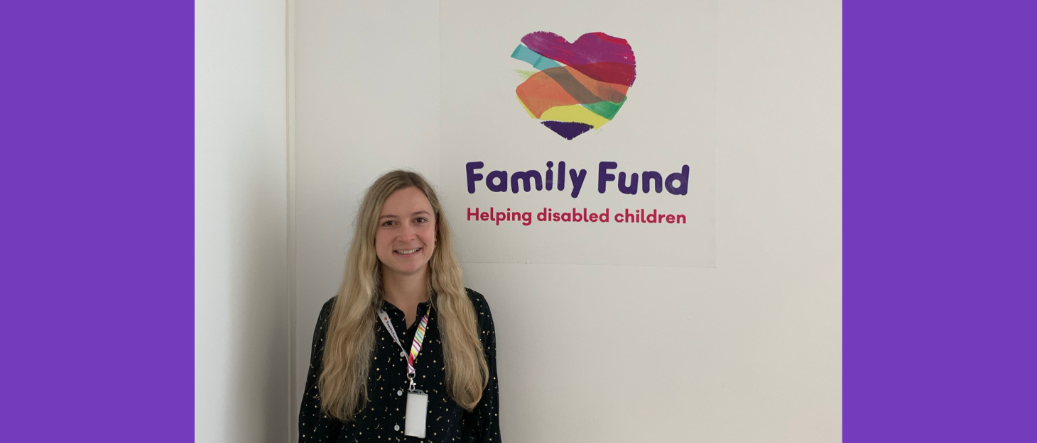 A photograph of Angelika, Marketing and Communications Apprentice in front of a wall with the Family Fund logo on in the office
