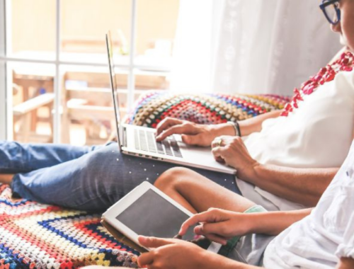 A mum sitting on a sofa with her feet up using a laptop, next to her a boy on a tablet