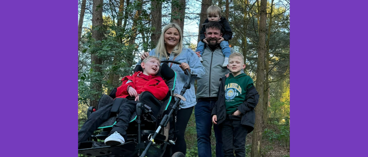 Mason, his brothers and parents are at Centre parcs walking amongst the trees on a path. They are all smiling at the camera. Mason is in a specialist pram, and Arthur is on Kris' shoulders. Archie is stood next to Kris, who has his hand on his shoulder. Jess is pushing Mason.