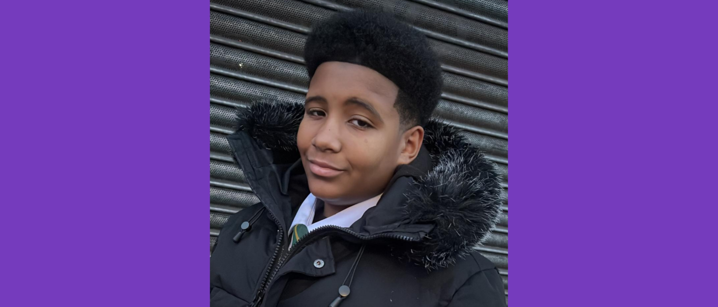 Derion is wearing a coat with a furry hood, and is smiling with a closed mouth at the camera. He has dark skin and black, freshly cut hair.