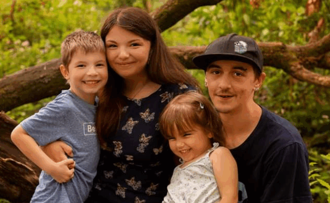 Daniel and Aria are on a family photoshoot with their children Jago and Hazel. They are surrounded by greenery, all close to one another and smiling.