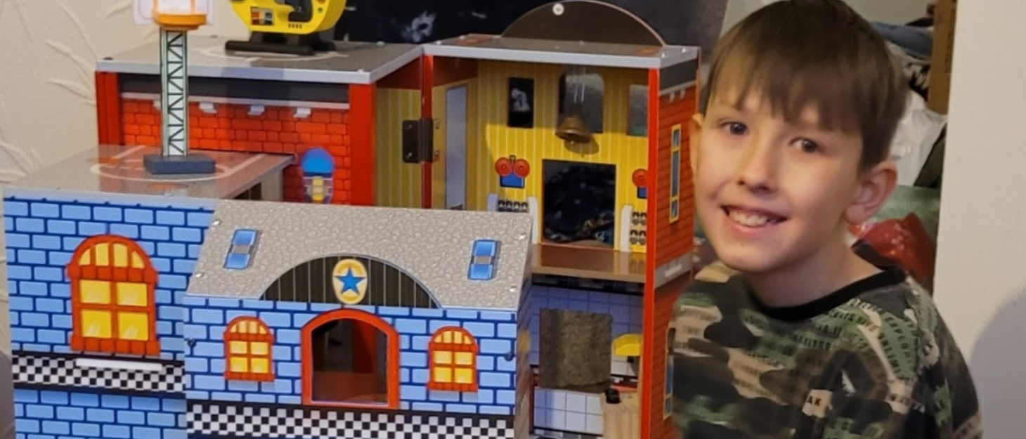 Corey is smiling, enjoying playing with his toy from Family Fund, an interactive police and fire station.