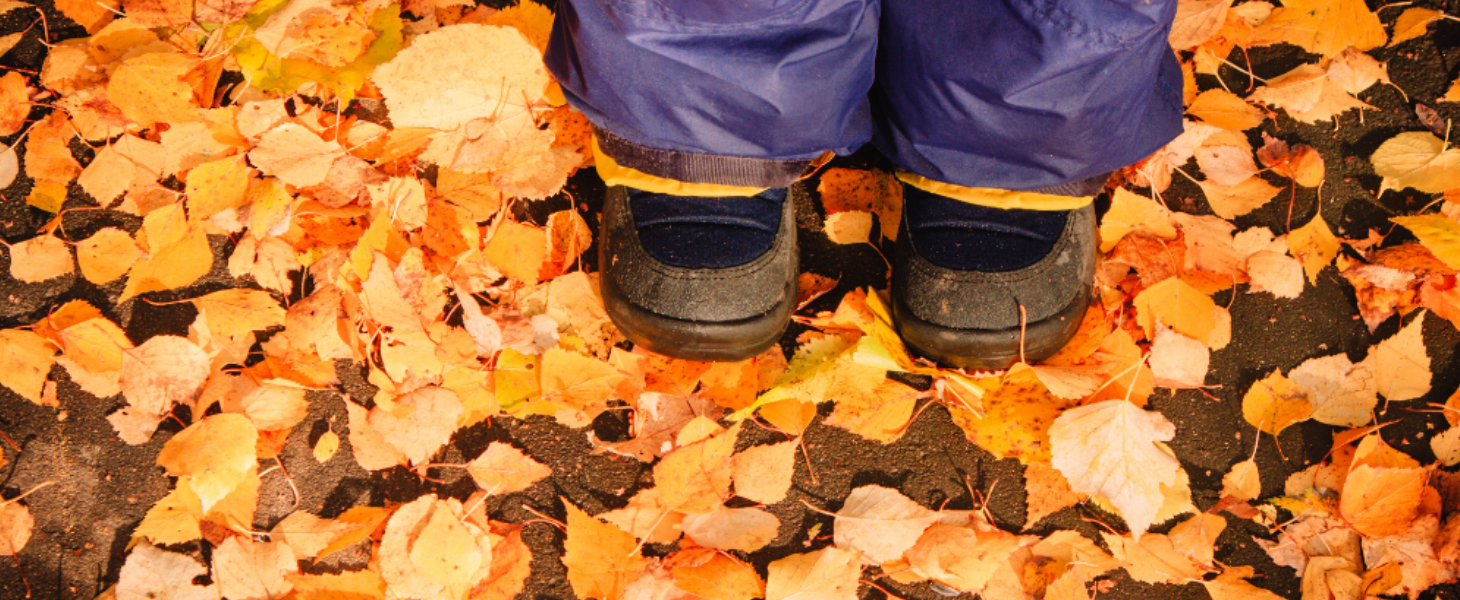 Close-up of a pair of black children's shoes standing on a bed of fallen autumn leaves.