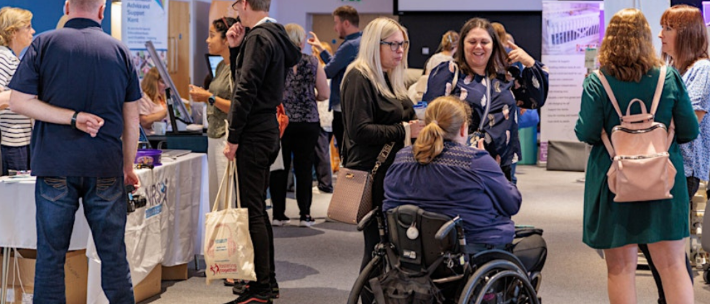 A photo of a large exhibition hall with stands and people walking around and talking.
