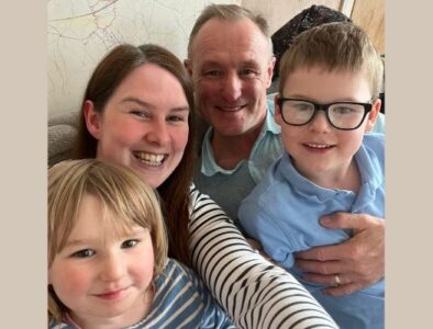 A family of four sat on a sofa looking at the camera and smiling.