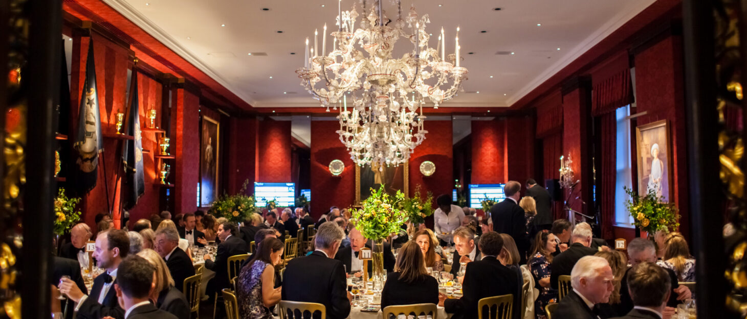 A room set up for a charity dinner at the Grocers' Hall in London. In the centre of the room is a large, ornate chandelier.