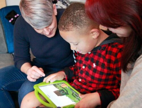 A boy using his iPad tablet with his mum and sister either side of him