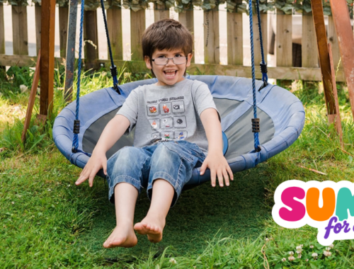 A young boy sits on a swing in his garden in the sunshine smiling. A logo in the bottom corner reads 'summer for everyone'.