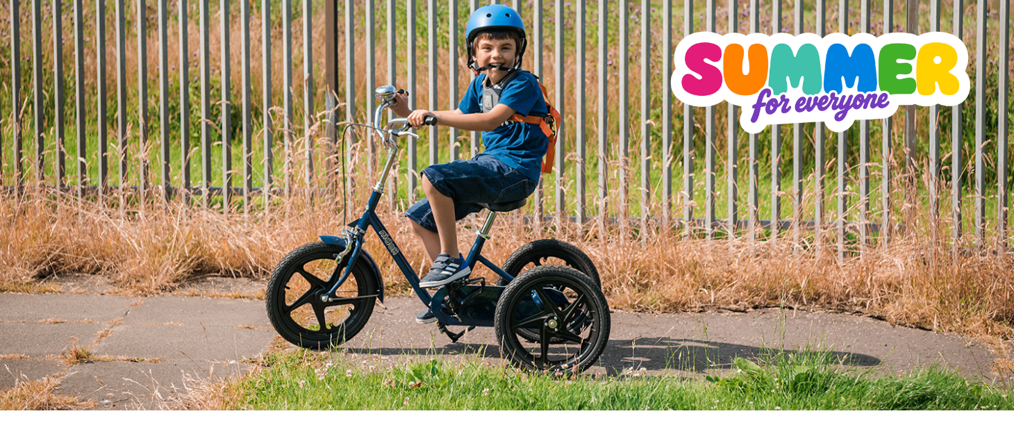 A young boy rides his adaptive bike outside wearing a helmet and looking at the camera. In the top left corner a colourful logo says summer for everyone
