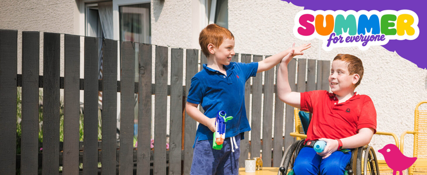 Two young brothers high five in the garden whilst playing games. One boy is in a wheelchair.