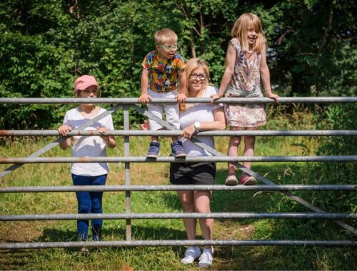 A family stood in the countryside at a metal gate looking into a field
