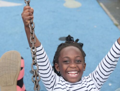 A young girl leaning back on a park swing with her feet in the air