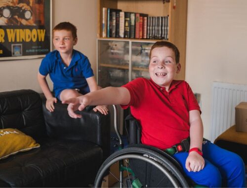 Two brothers in a living room, one in a wheel chair pointing outside