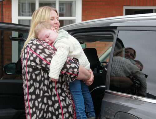 Mother holding her toddler about to put him into the back of a car