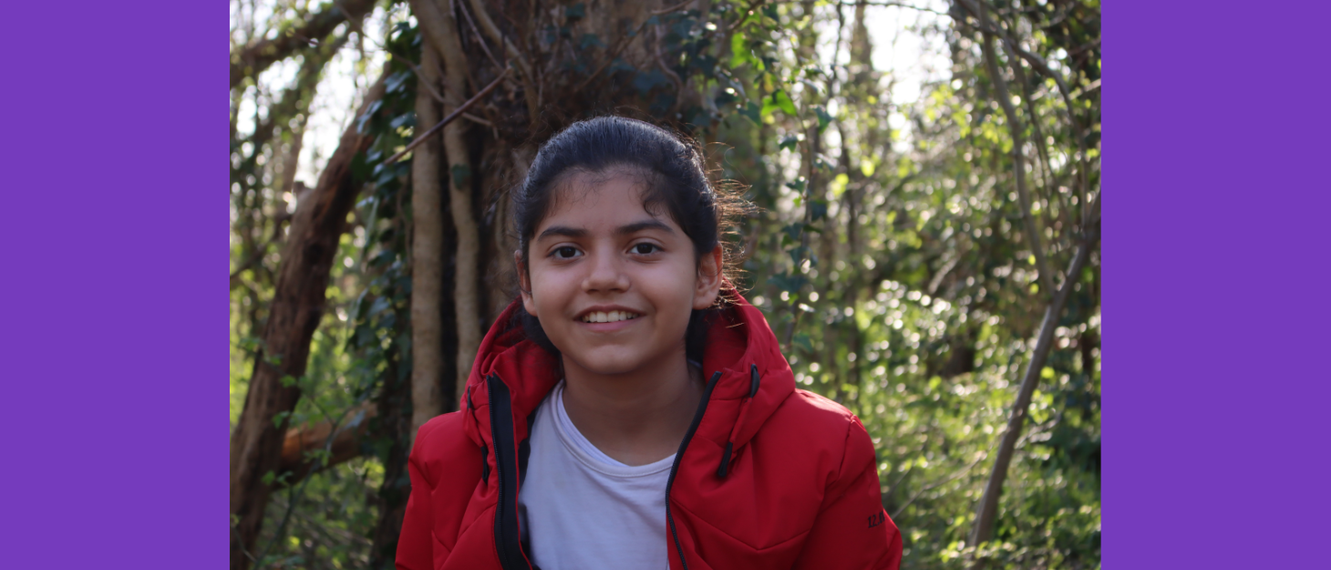 A young girl in a wooded area wearing red coat