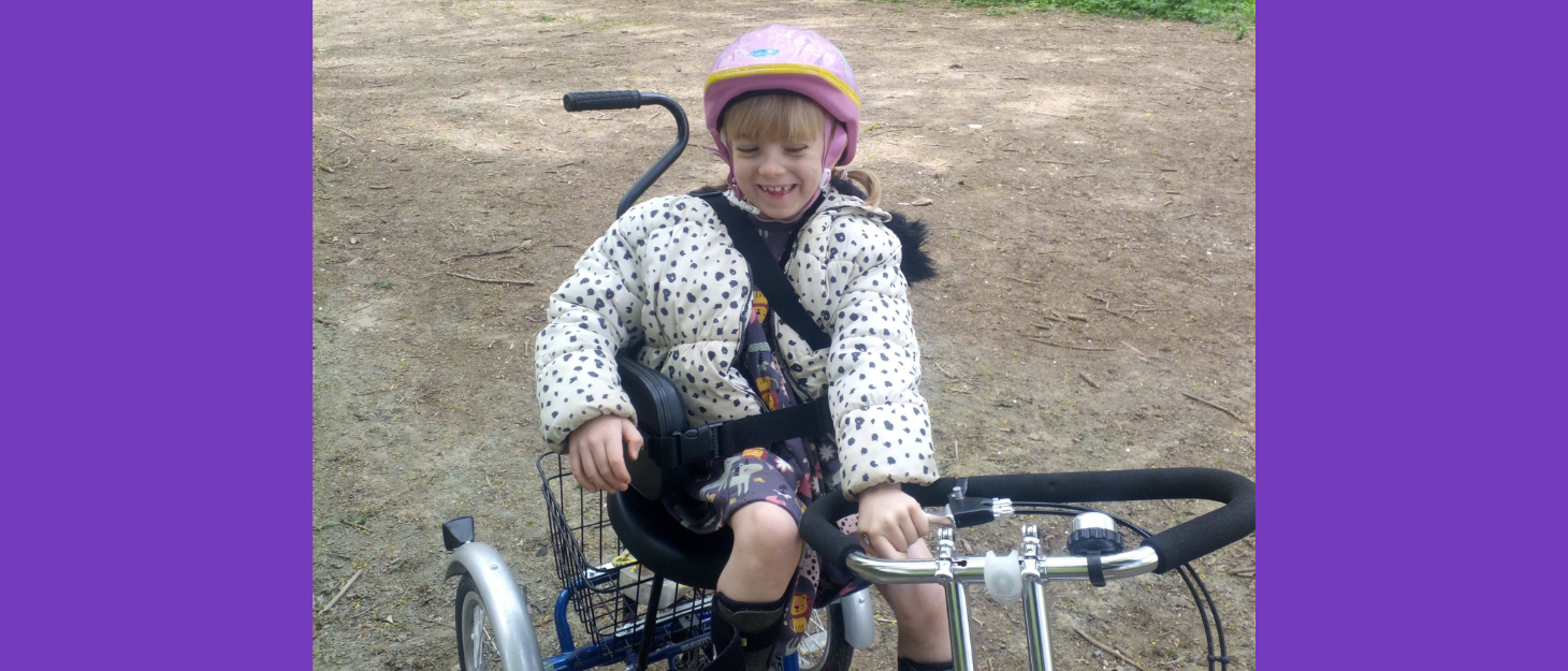 girl with pink helmet on rides on specialist tricycle