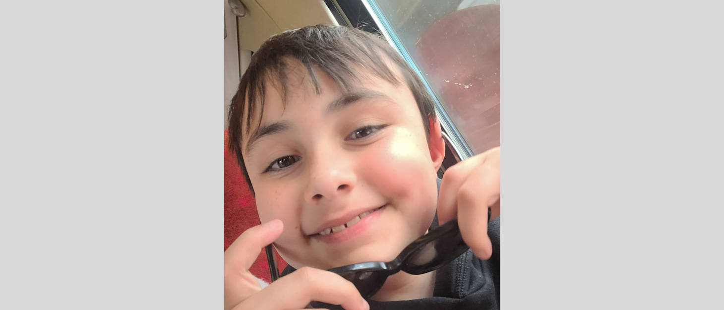 boy holding swimming goggles smiles at the camera