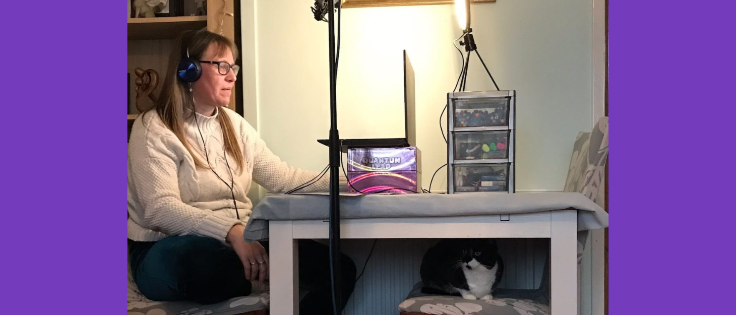 Woman sits on chair wearing headphones, looking at laptop