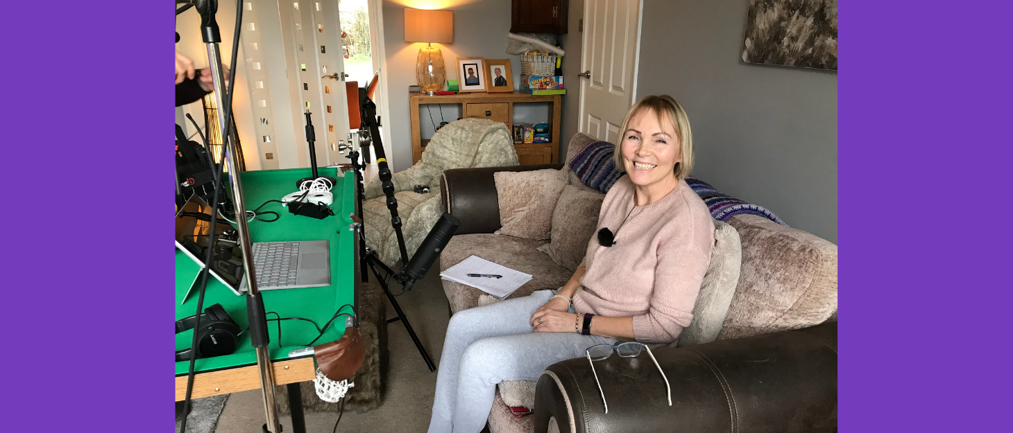 A woman sits on a sofa with a microphone and a laptop.