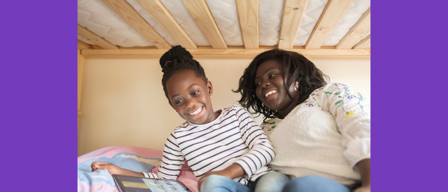 Mum and daughter smile as they look at a tablet on the bed