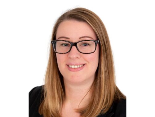 A woman with long blonde hair and dark framed glasses