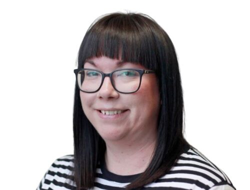 A woman with dark straight hair and dark framed glasses