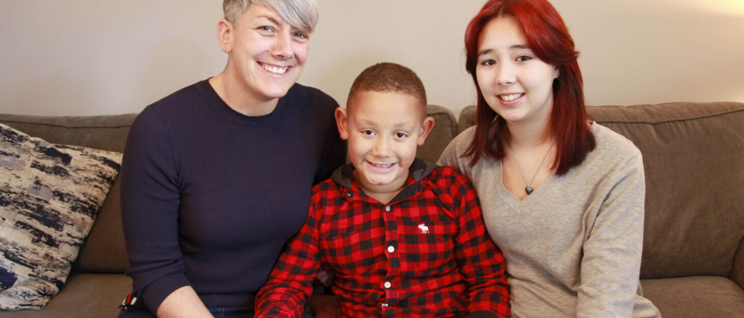 A mother sitting on a sofa with her son and teenage daughter beside her