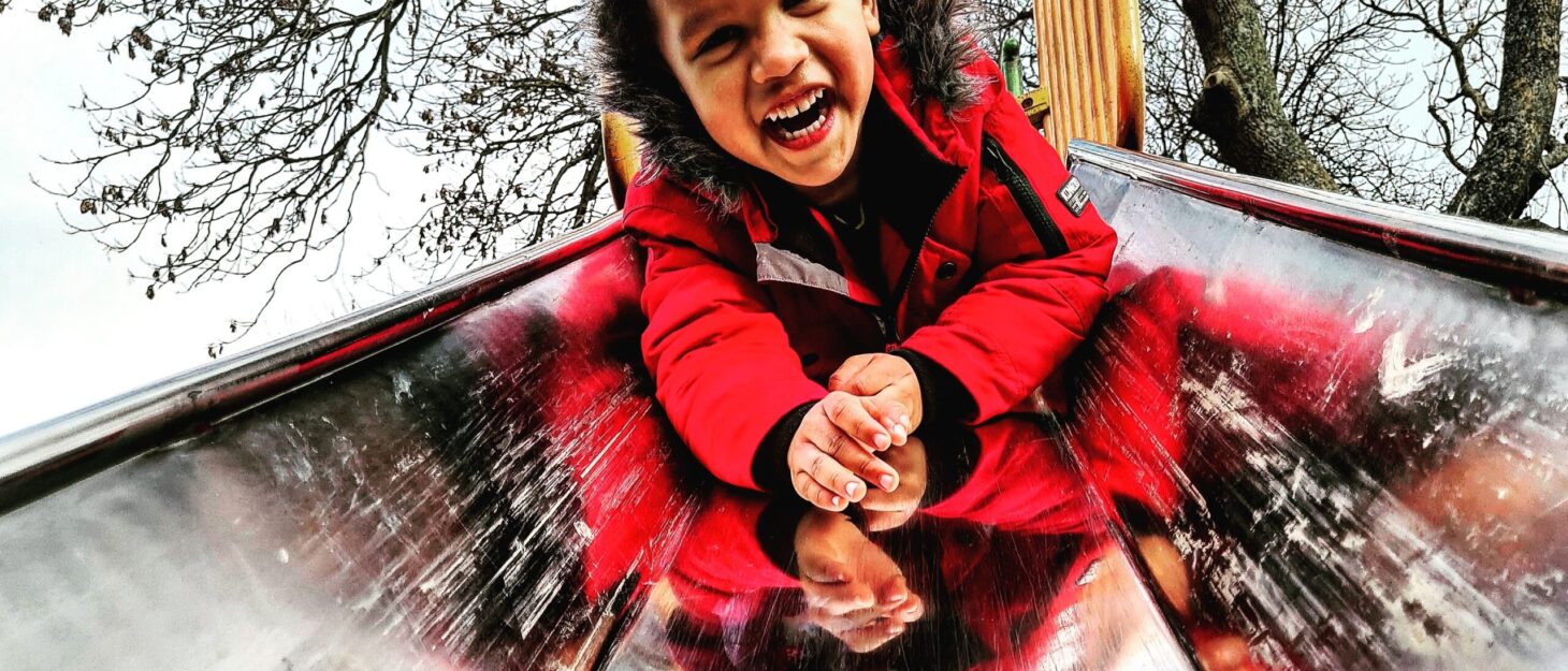 A little boy in a red coat sliding down a metal slide