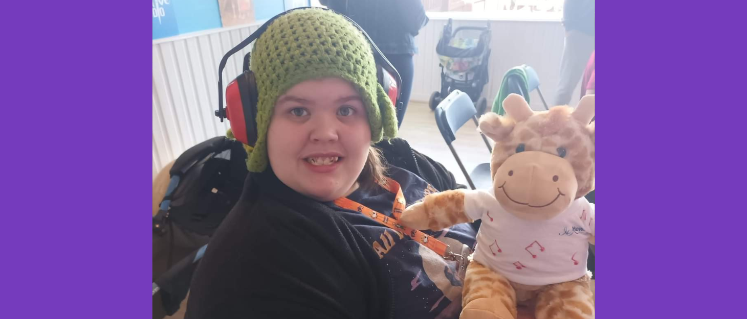 Young woman wearing a green hat smiling into the camera whilst holding a toy giraffe.
