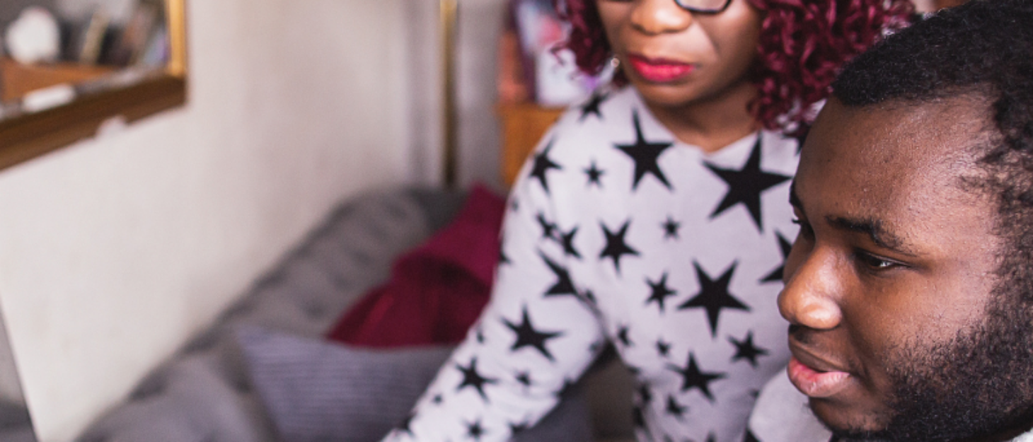 a mum wearing glasses and a starred tee shirt is looking at her computer, with her teenage boy next to her