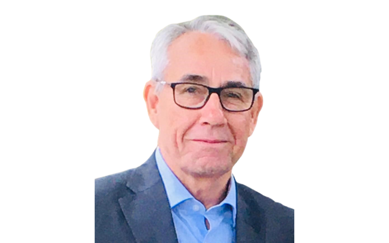 A man with white hair and wearing a blue shirt and black glasses is smiling