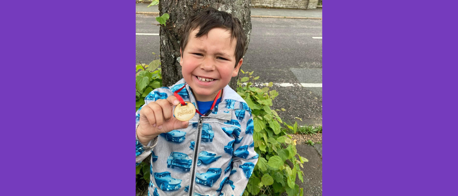 Cody standing in front of a tree holding a medal for reading.